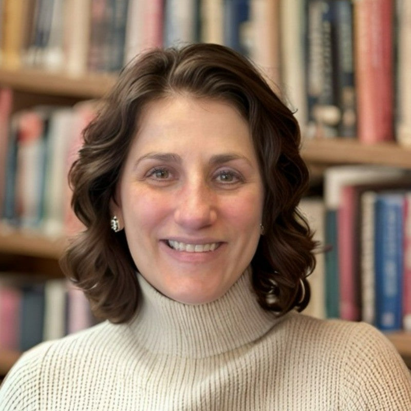 Leana Levin in a white turtleneck sweater standing in front of bookshelves.